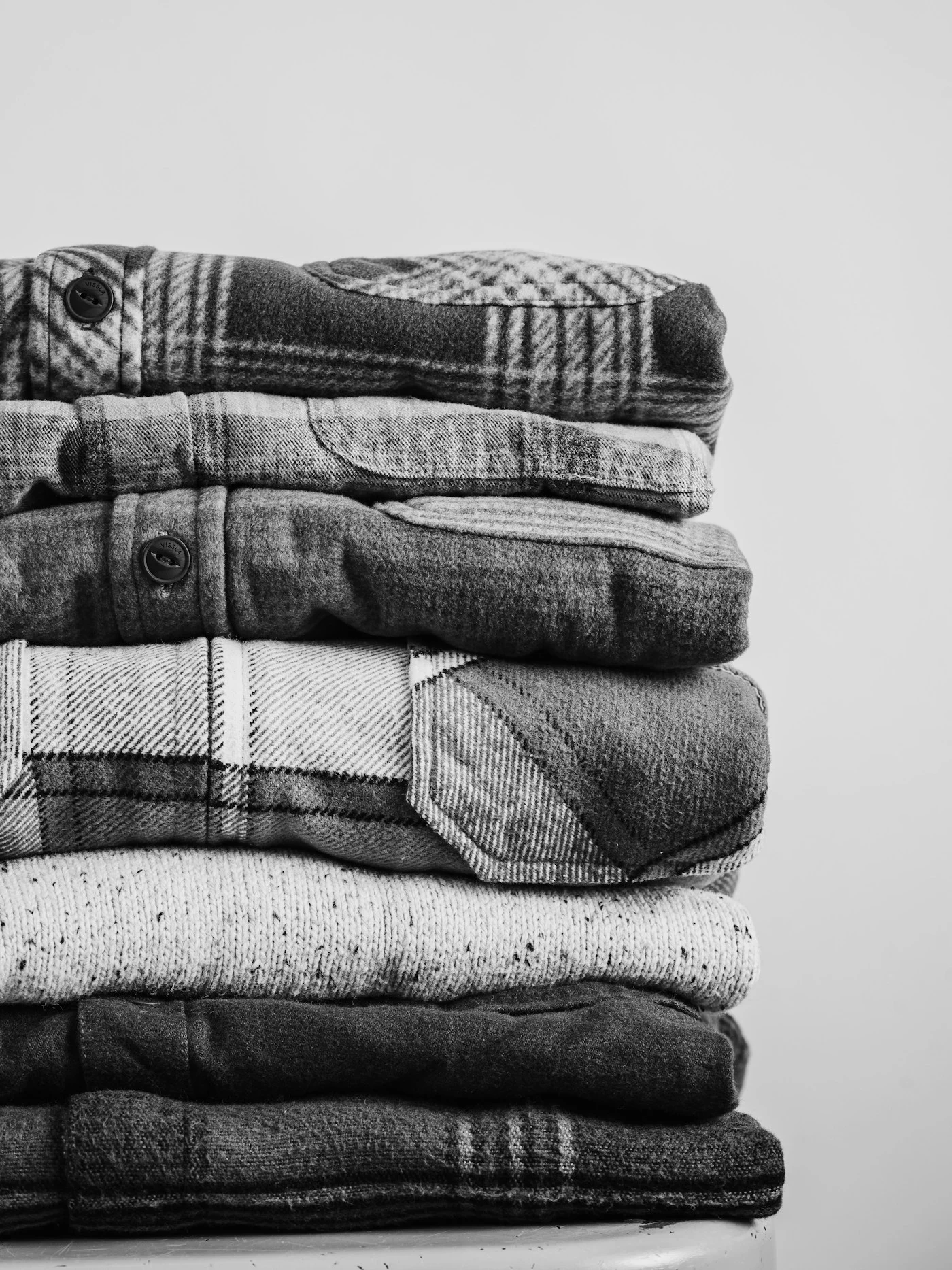 A stack of folded plaid flannel shirts in black and white — material reference