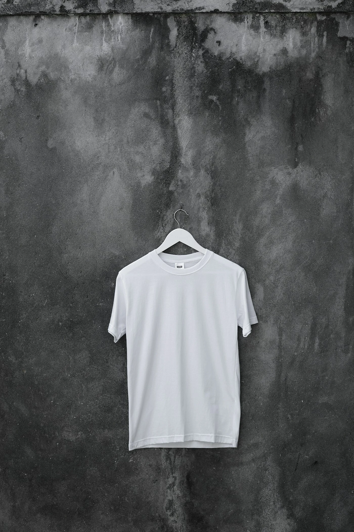 A white crewneck T-shirt hanging against a textured wall — style reference